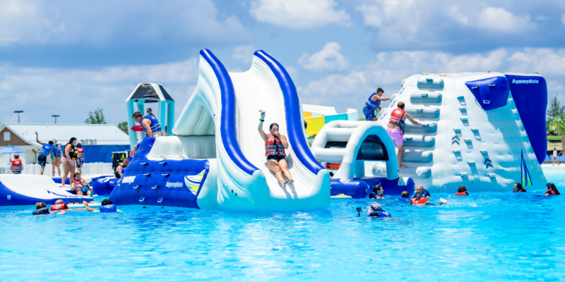 A girl sliding down an inflatable slide attached to a water obstacle course in the blue waters of the lagoon.